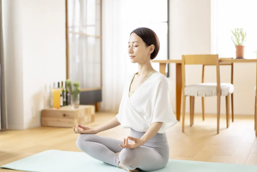 A woman meditating in a bright room with natural light.
