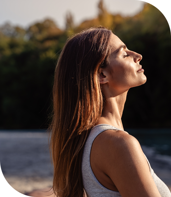 A woman with closed eyes enjoying sunlight outdoors.