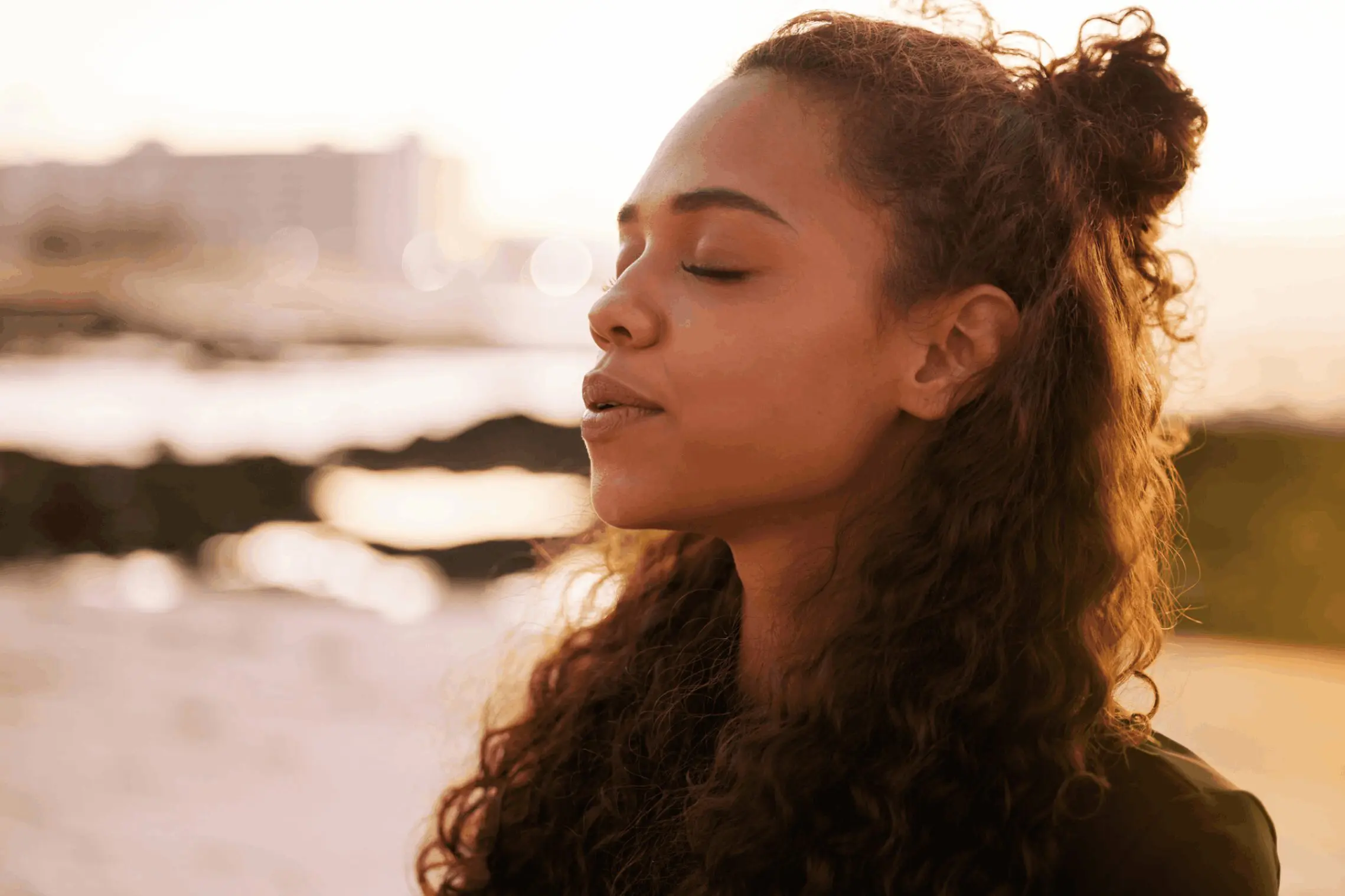 A woman with curly hair enjoying a serene moment by the water.