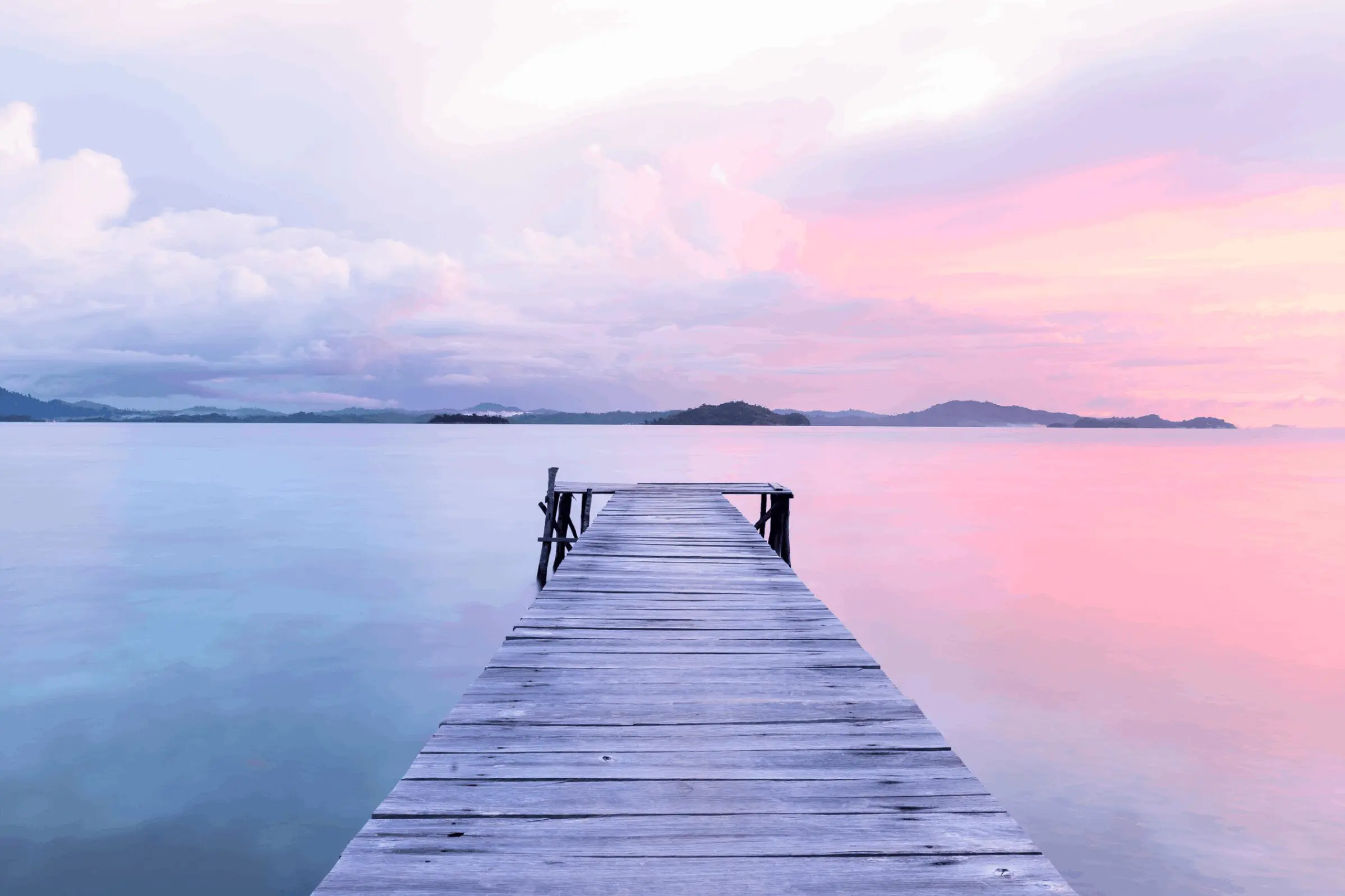 A wooden pier extending into calm, pastel-colored waters at sunset.
